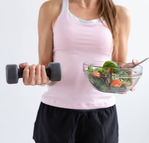woman-holding-a-barbell-and-a-bowl-of-vegetables mobile