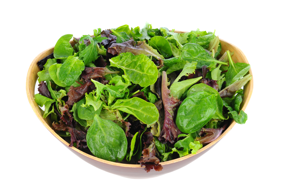 A wooden bowl filled with mixed green leafy vegetables 