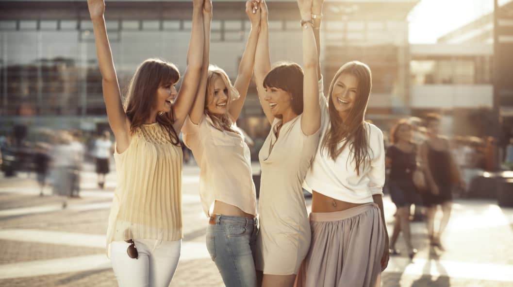 four women raising each other's hands in the middle of a street