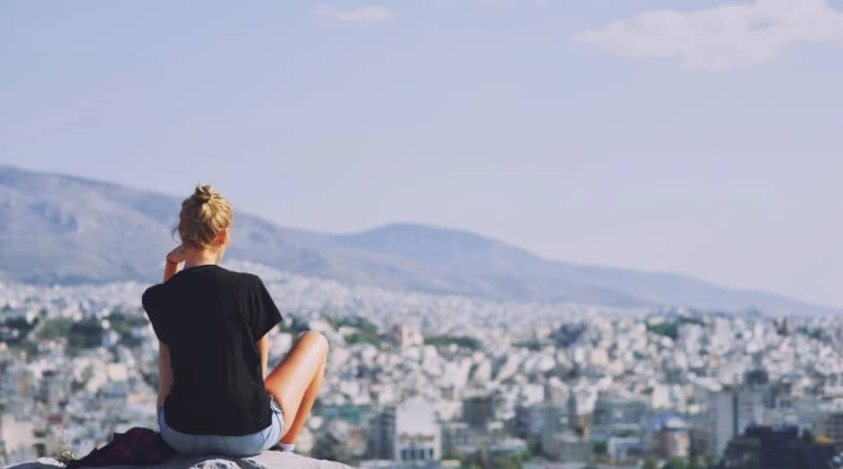 woman sitting on an edge of a cliff while looking at an aerial view of the city