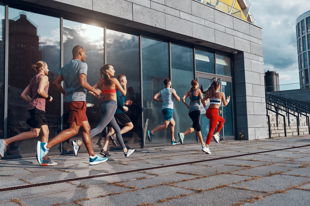 Group of people running outside, next to a modern building with glass windows on a cloudy day.