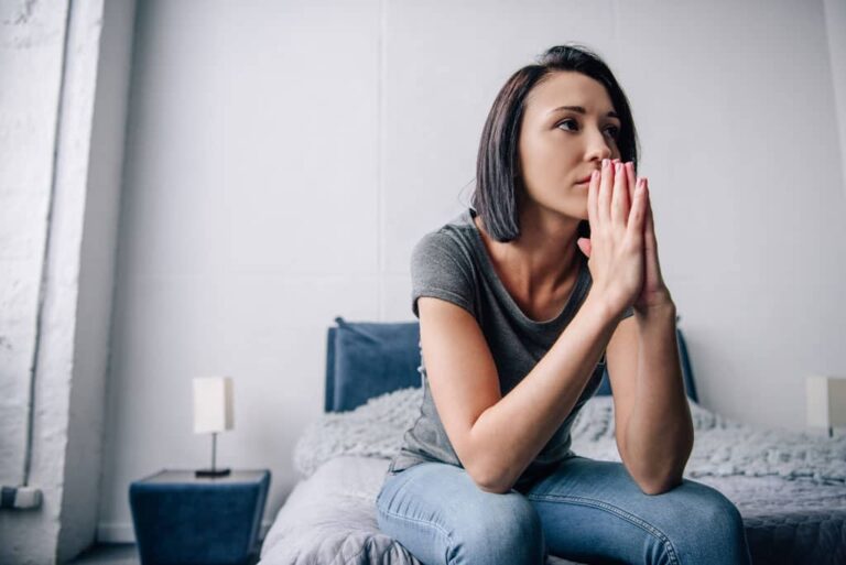 woman sitting on the edge of a bed with hands together
