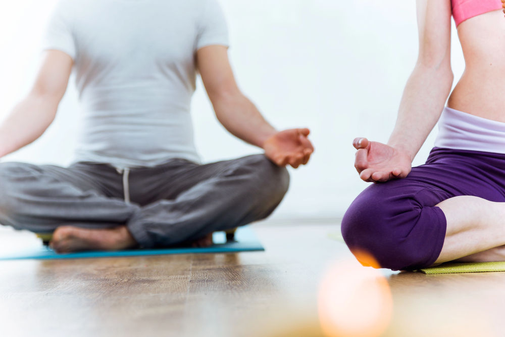 Two people sitting cross-legged on yoga mats in a meditative pose with their hands resting on their knees