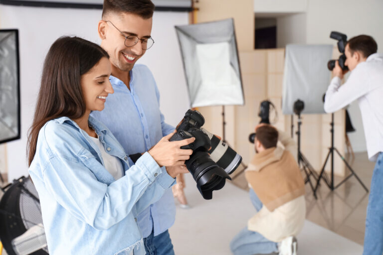 A man and woman look at a camera screen in a photography studio, while two other people work with cameras in the background.