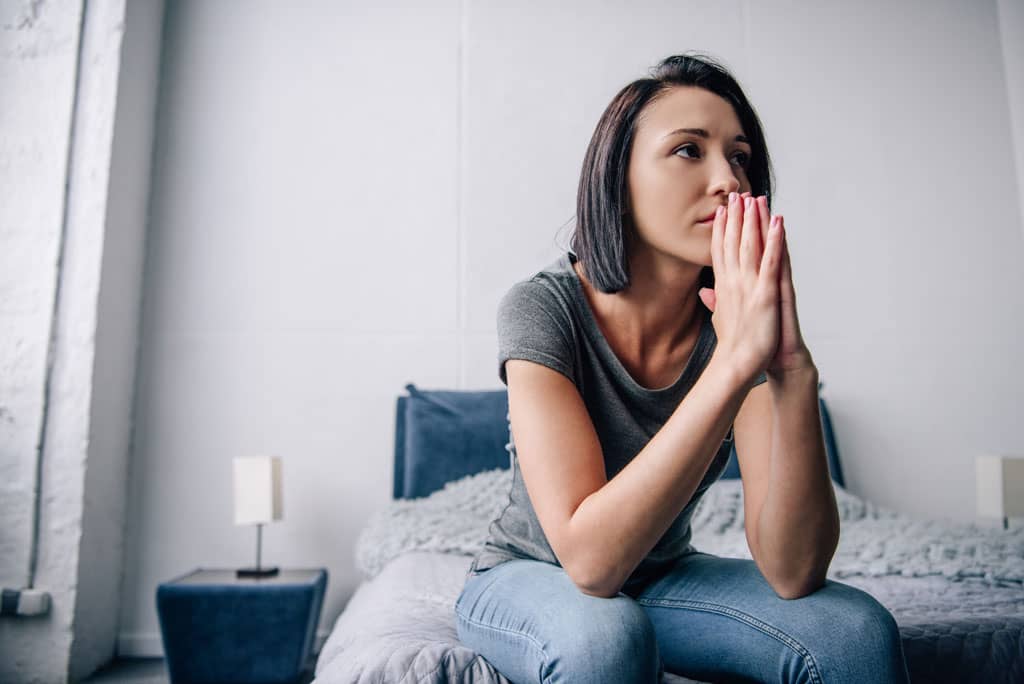woman sitting on the edge of a bed with hands together