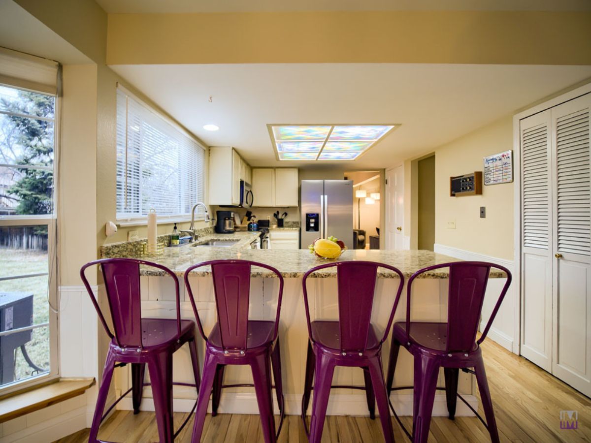 A modern kitchen with granite countertops, four purple metal barstools, stainless steel appliances, and a lemon on the counter.