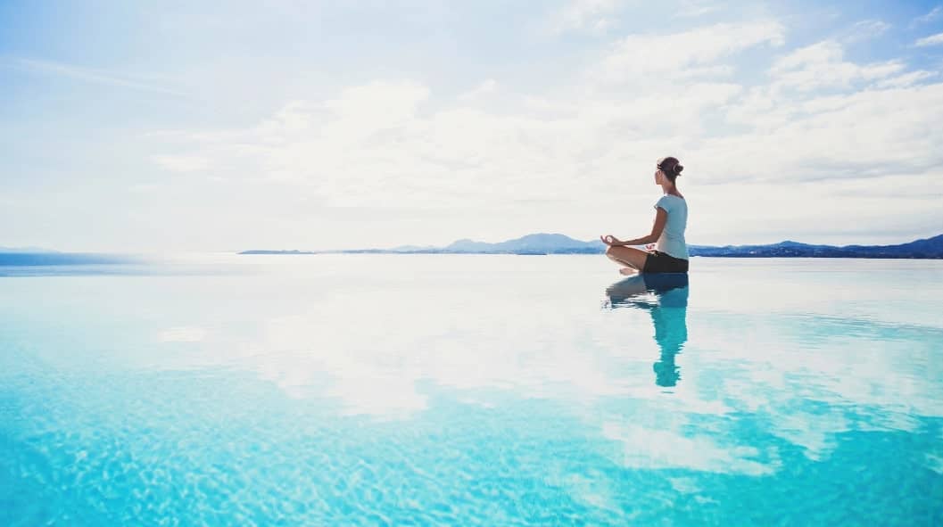 woman doing a seated yoga pose at the side of an infinity pool