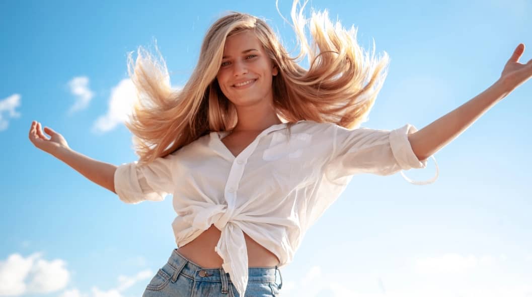 Beautiful young blonde girl with flowing hair and dimples against the blue sky and the sun