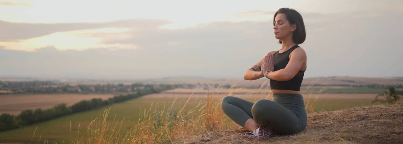 Calm serene sporty young woman meditate while sitting in namaste pose with eyes closed