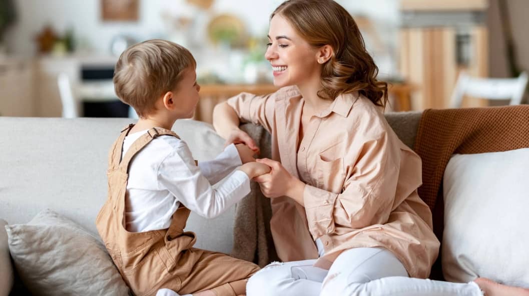 Delighted mother smiling and playing with son while resting on couch at home together