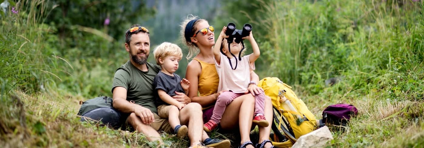 Family with small children hiking outdoors in summer nature, sitting and resting