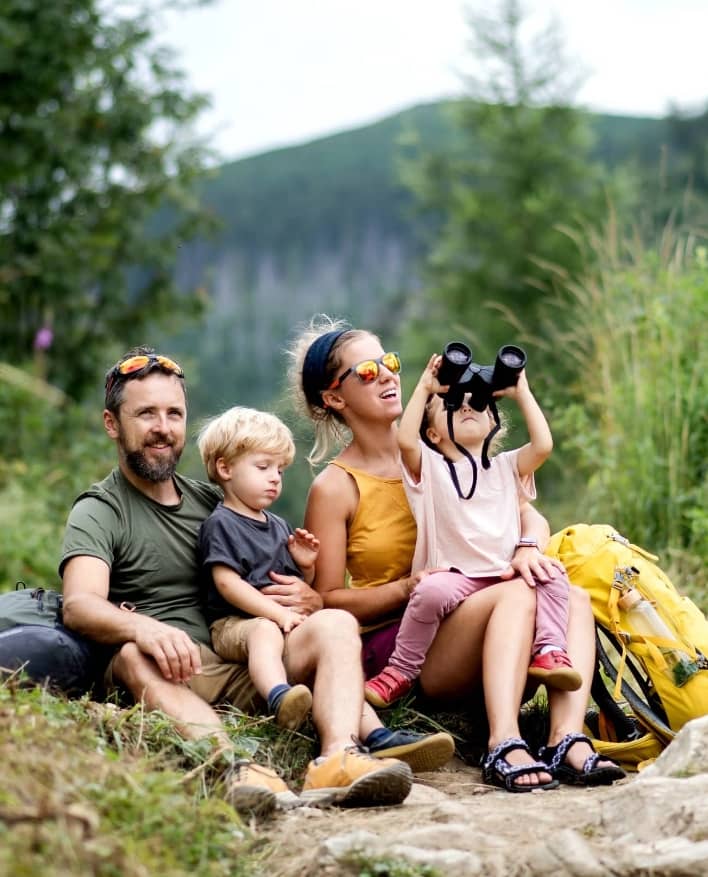 Family with small children hiking outdoors in summer nature, sitting and resting