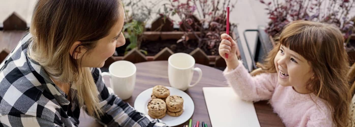 Mother And Daughter Drawing With Pencils Helping Her Child Draw A Picture In Cafe