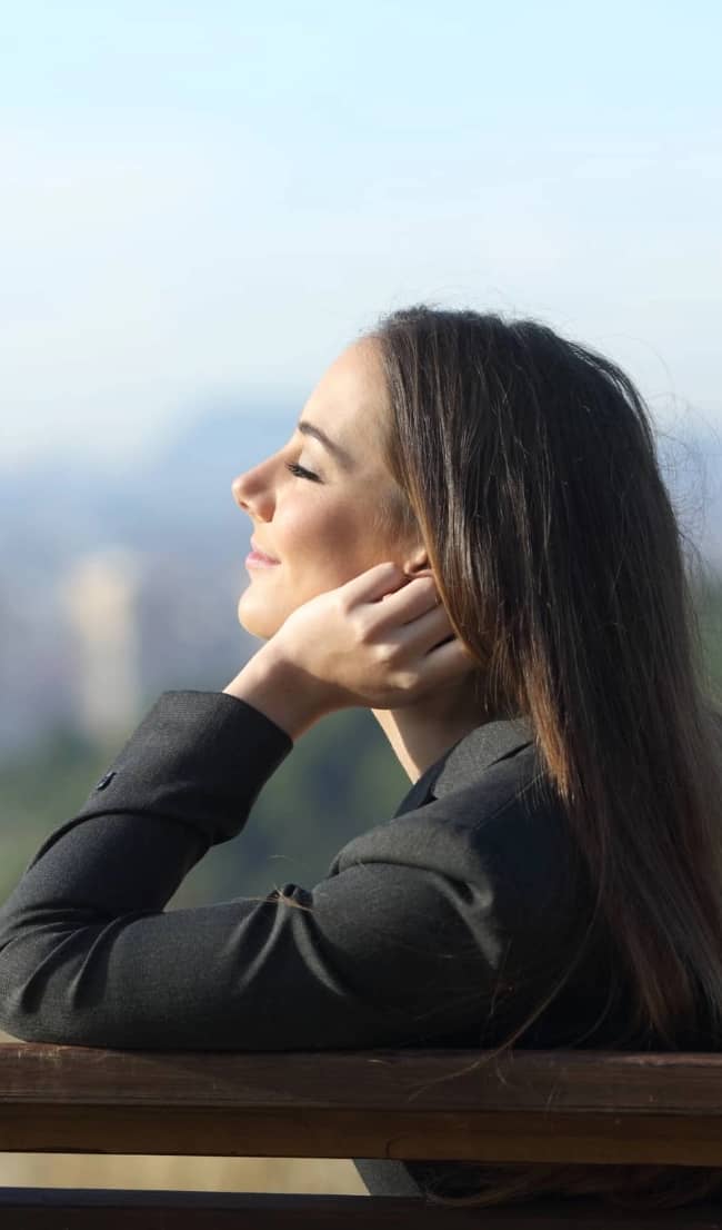side view portrait of a businesswoman relaxing sitting on a bench with eyes closed and a city in the