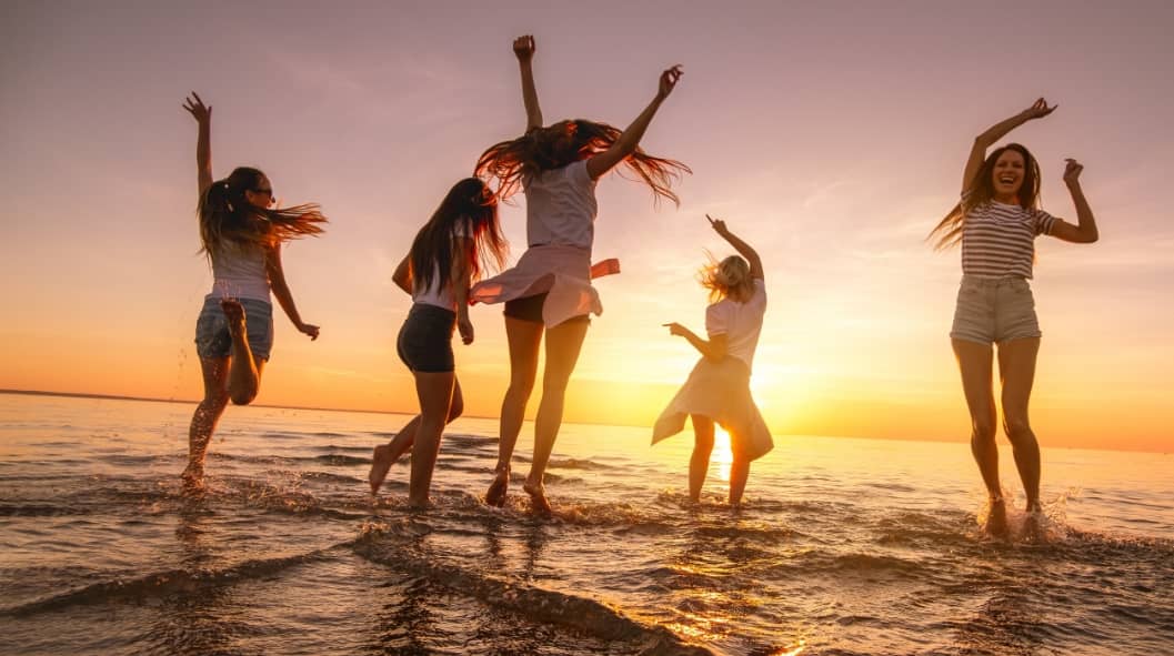 Group of happy young girls are having fun and dancing at sunset sea beach