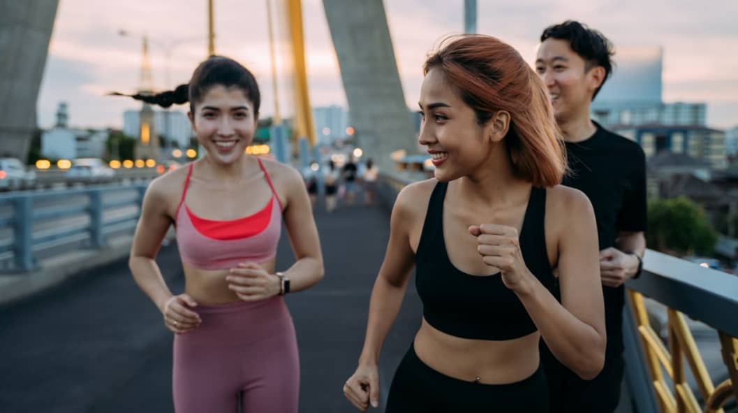 Happy Asian female and male friends in sportswear running and jogging at city bridge for a fit and healthy lifestyle - friendship and healthy