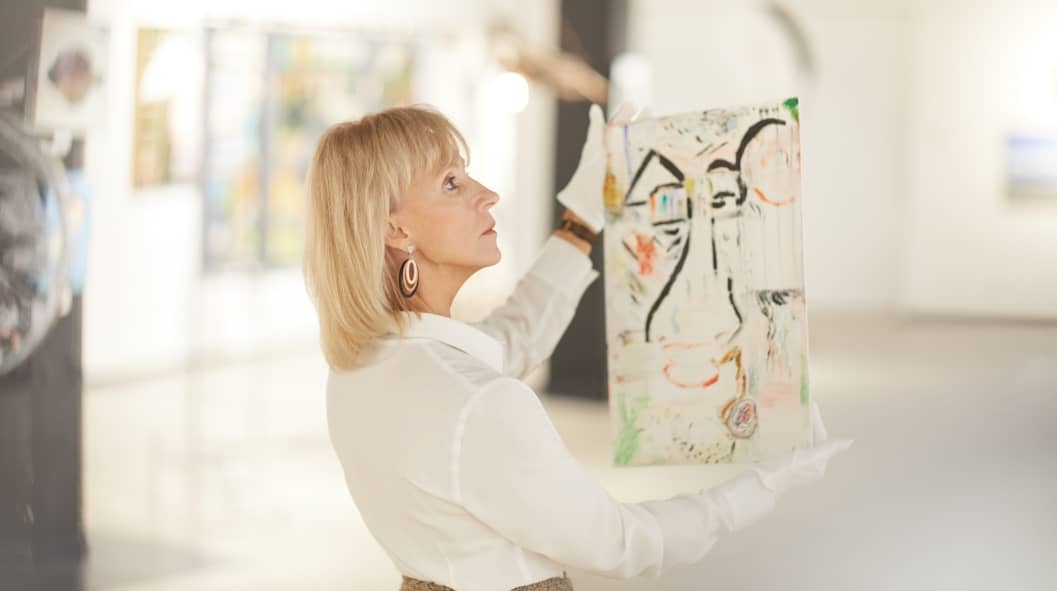 Portrait of female art expert holding painting while appraising works in modern gallery or museum
