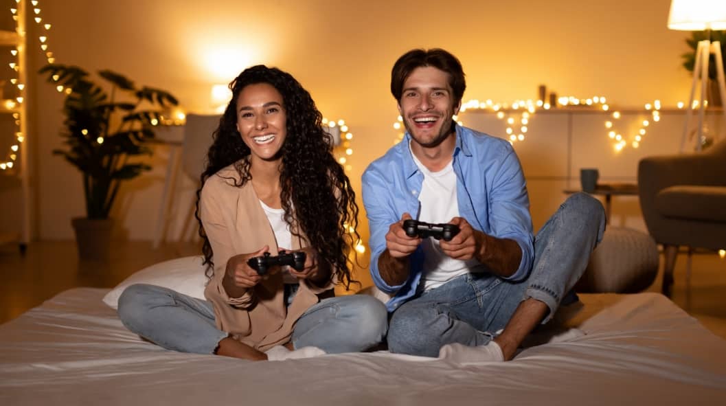 Young Husband And Wife Playing Videogame Sitting In Bedroom