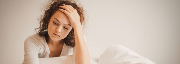 Sad young woman sitting on bed, feeling upset with hangover