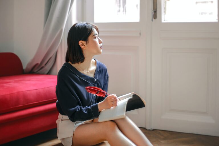 woman writing on her journal while looking at the window