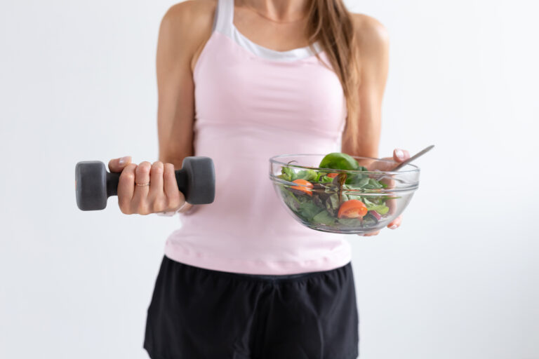 woman holding a barbell and a bowl of vegetables