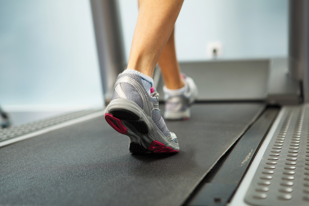 A person walking on a treadmill, wearing grey and pink athletic shoes.