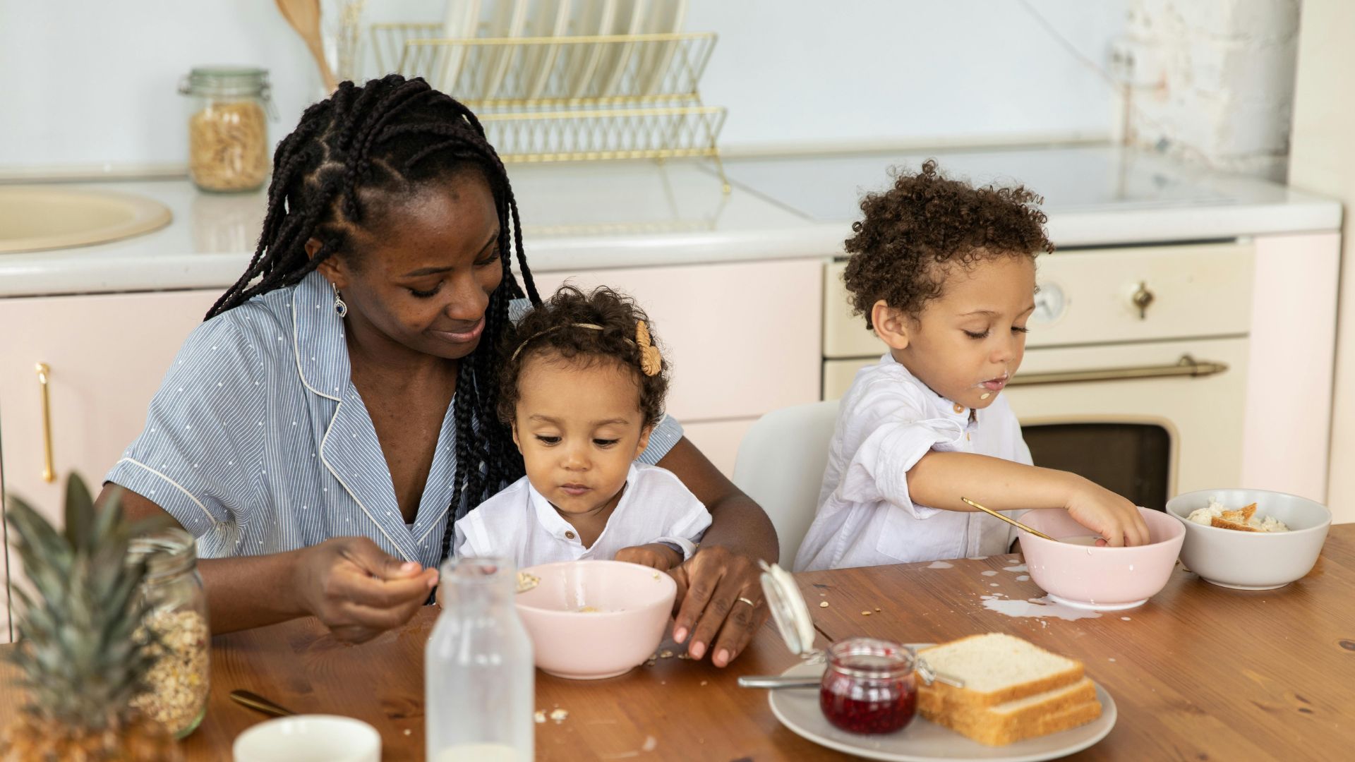 A woman and two young children sit at a kitchen table eating breakfast, enjoying bowls, bread, and jam—one of the many things to do instead of drinking.